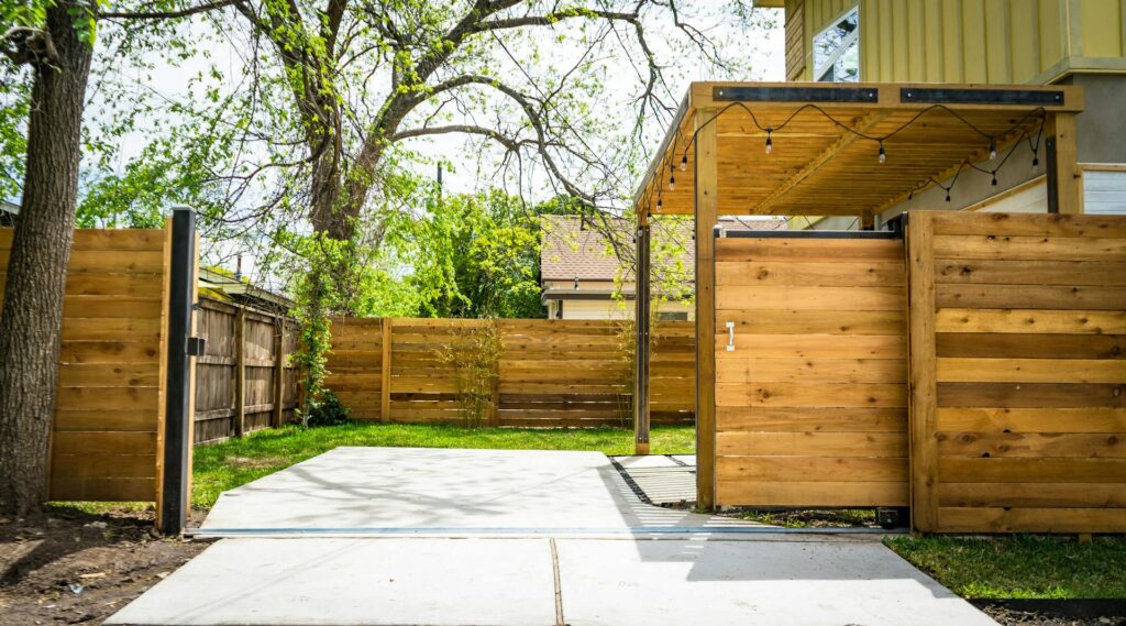 A backyard with a wooden fence and pergola, featuring a large tree with branches extending over the property, possibly requiring tree trimming.